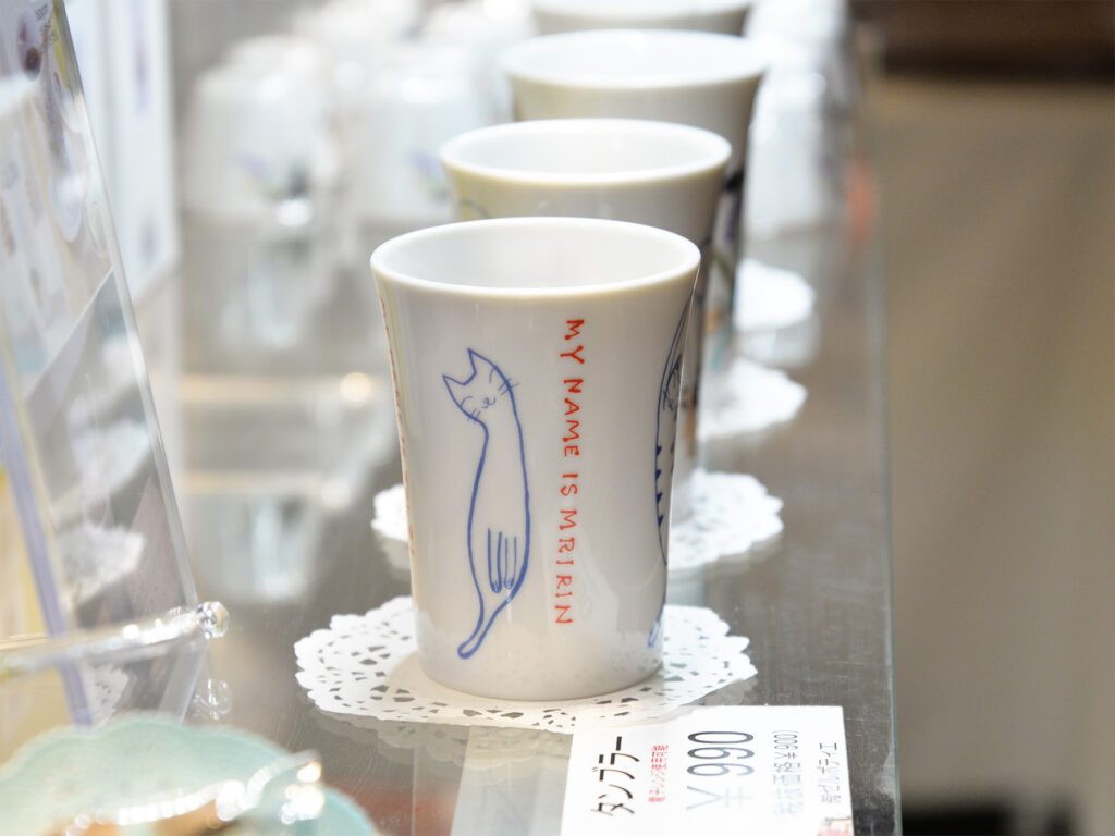 白い美濃焼製の陶磁器、タンブラーにブルーの猫のイラストが描かれた可愛いタンブラーの販売の様子の画像