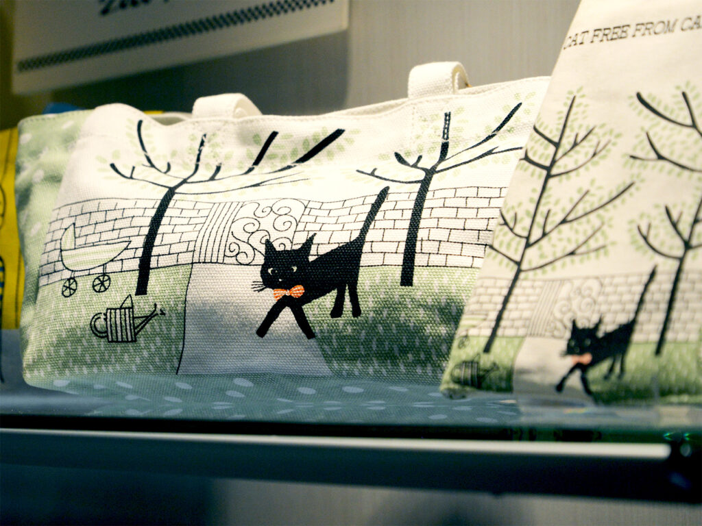 雑貨デザイナーシンジカトウさんが帆布の生地のショートバッグに可愛い猫のイアスとが描かれたランチバッグの画像です。