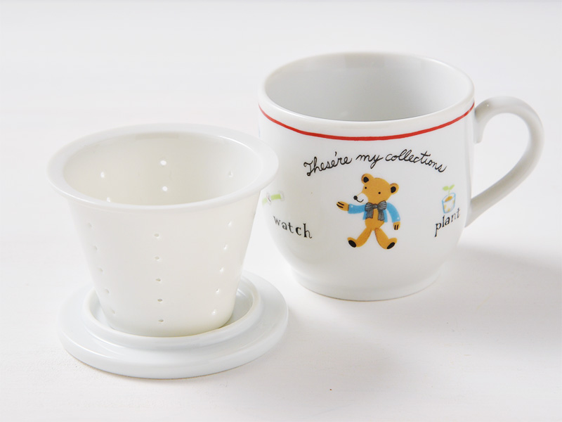 美濃焼の白いハーブマグカップにおしゃれな可愛さのくまのイラストが描かれているハーブマグカップから蓋と茶こしを取りだし、蓋の上に茶こしを置いている使用シーンの画像です。
