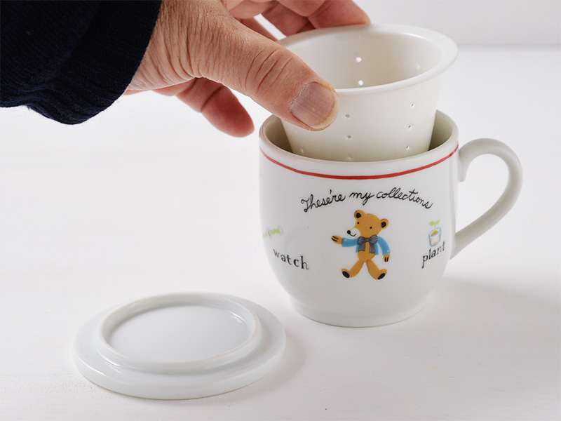 美濃焼の白いハーブマグカップにおしゃれな可愛さのくまのイラストが描かれているハーブマグカップの蓋を外し次に茶こしをマグカップから取り出している画像です。