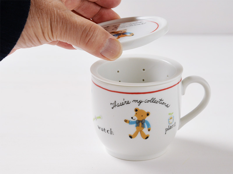 美濃焼の白いハーブマグカップにおしゃれな可愛さのくまのイラストが描かれているハーブマグカップの蓋を手で持ち上げている画像です。