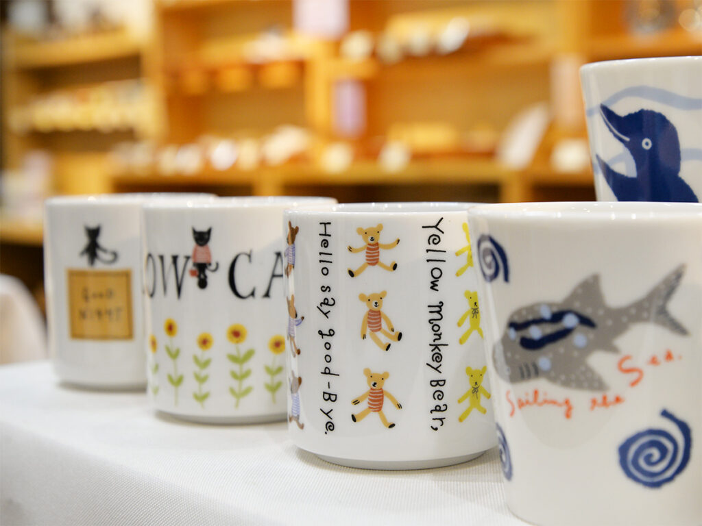 可愛い猫やくまが白い陶磁器製のマグカップにデザインされた商品の販売の様子の画像です。