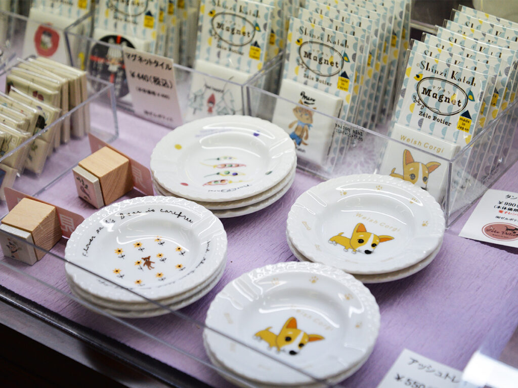川島パーキングエリアの岐阜おみやげ川島店で販売されている雑貨デザイナーシンジカトウさんがデザインしたくまのイラストや猫のイラストが描かれた小皿やタイルの画像です。