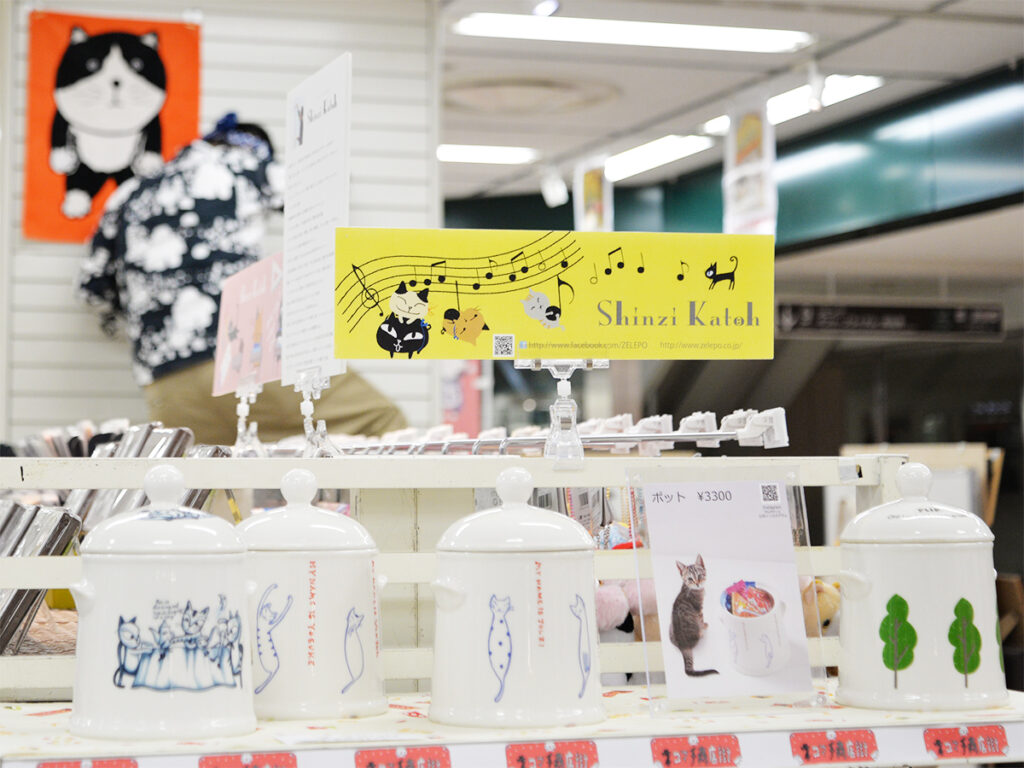 ハンズ名古屋店で開催中のネコマチ商店街での雑貨デザイナーシンジカトウさんデザインした可愛い猫のイラストが描かれた美濃焼製の陶器のポットの販売の様子の画像です。