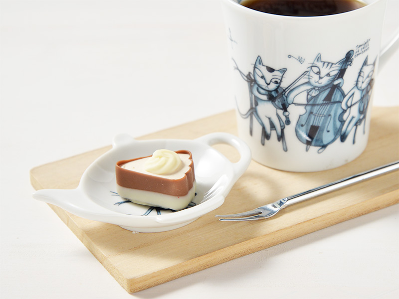 ユーモレスクシーリーズのティートレー、小皿とにチョコレートを盛り付け、同じシリーズのマグカップにコーヒーを淹れてテーブルの上に置いてある様子の画像です。