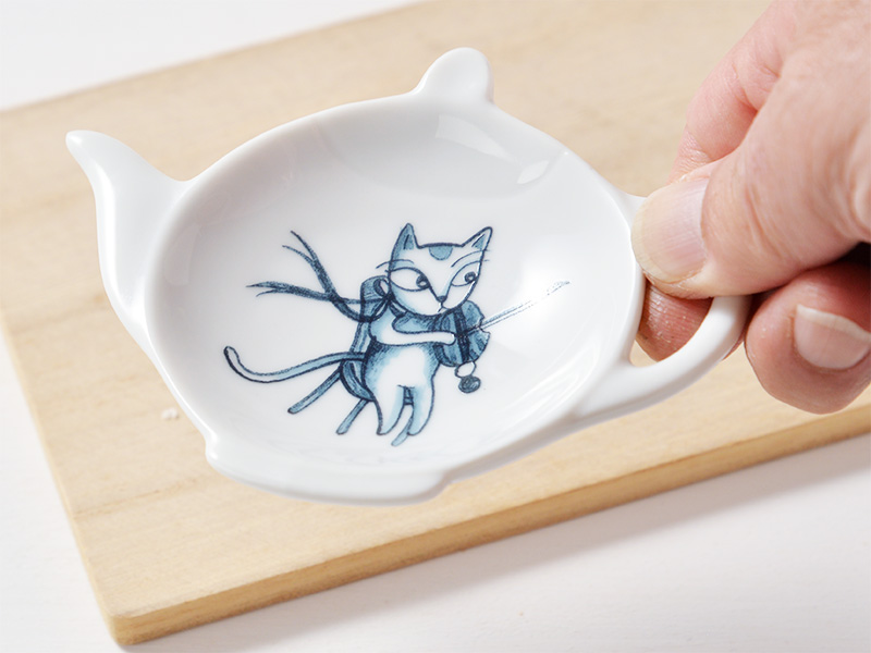 直径10cm位の大きさのティーポットの形を小皿にしたティートレーです。
白い小皿に紺色で
バイオリンを練習している猫が描かれた陶器の小皿の画像です。