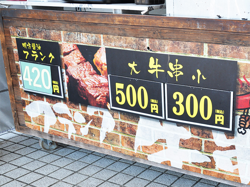 「大 牛串 小」と書かれた木製のフードスタンドのメニュー看板。大きな文字で価格が「500円」と「300円」と表示されています。