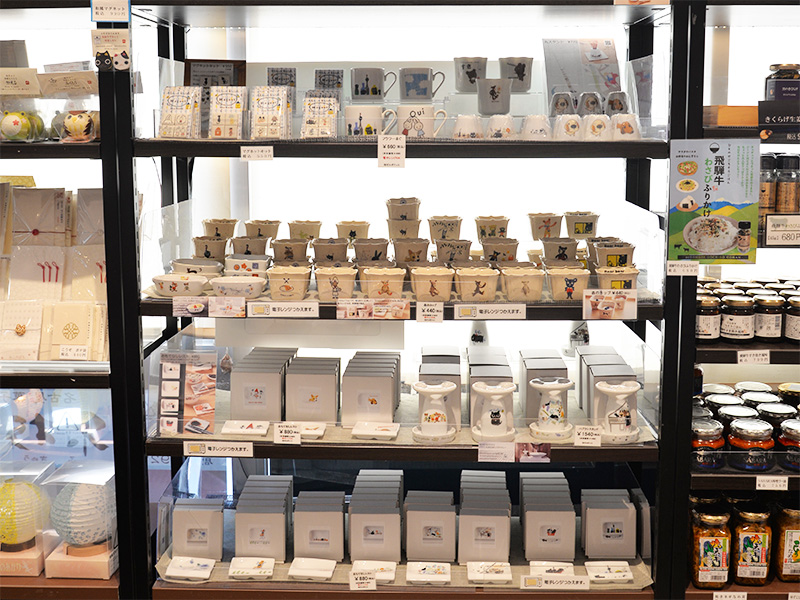 ゼルポティエの美濃焼商品が並ぶ棚のクローズアップ。猫のイラストが描かれたマグカップや小皿、ハブラシスタンドなどが並んでいます。