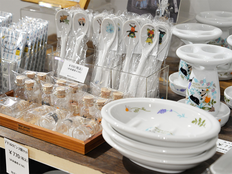 店頭のディスプレイ。透明なケースの中に、様々な動物のイラストが描かれた白い陶器製のスプーンが整然と並べられている。手前にはコルクの蓋が付いた小さなガラス瓶が木製の箱に多数入っており、奥には猫のイラストが描かれた白い歯ブラシスタンドと、ラベンダーの絵柄の入った白い石鹸置きが重ねて置かれている。