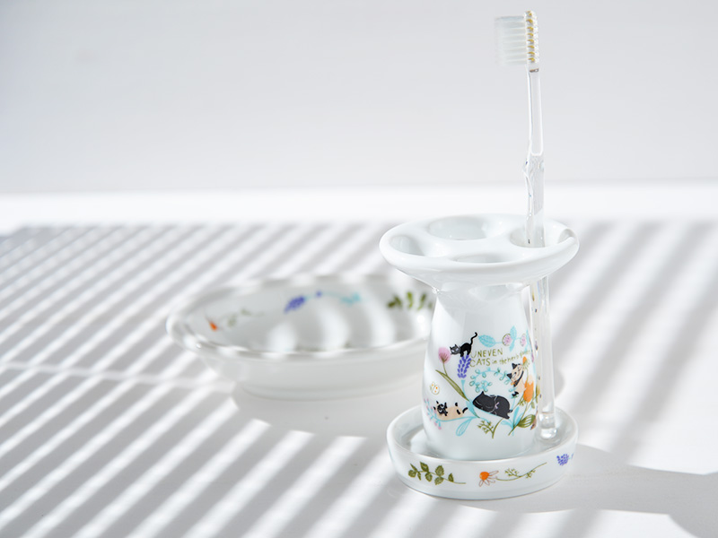 雑貨デザイナーシンジカトウが美濃焼製の白い陶磁器製のハブラシスタンドに可愛い猫のイラストをデザインした清潔感を感じさせるハブラシスタンドの画像です。