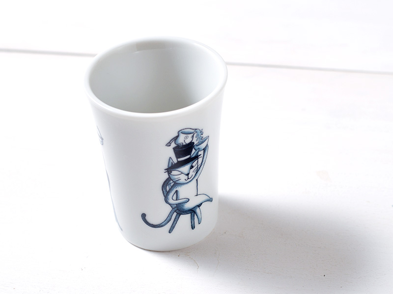 白い背景にタンブラーを斜めから捉えた写真。黒い帽子をかぶった猫のイラストが前面に描かれている。イラストは青い線画で、ユーモラスな表情をしている。