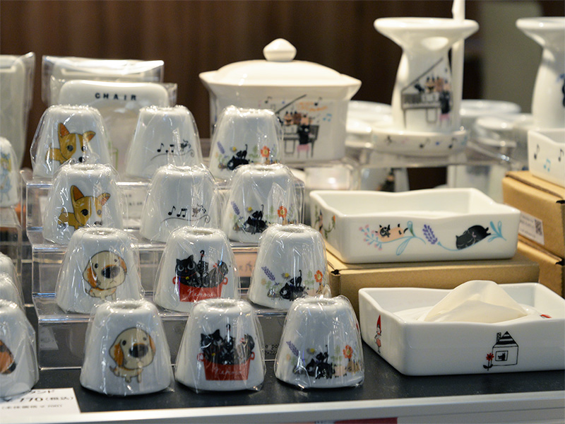 【商品クローズアップ】犬（コーギー、ゴールデンレトリバー）と猫（黒猫）のイラストが描かれた可愛いココットやミニ容器が並び、細部までデザインが楽しめる様子。
