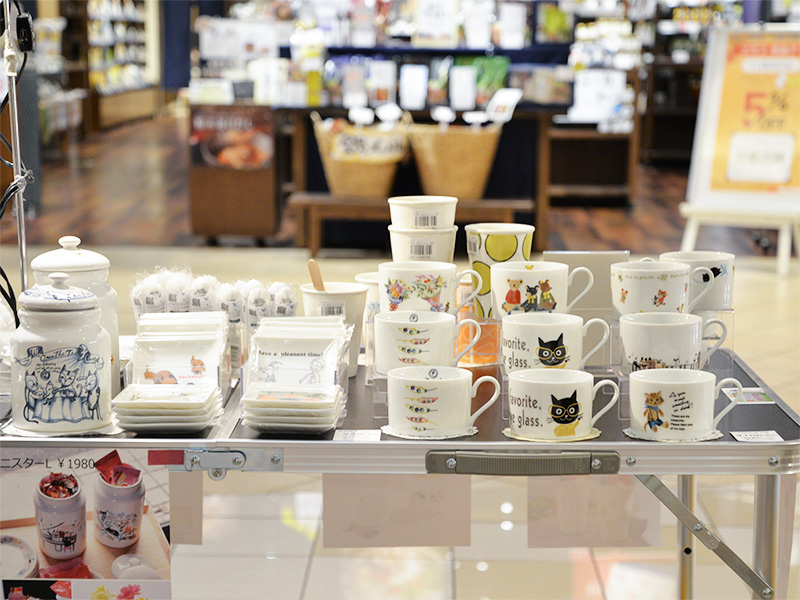 【商品陳列】シンジカトウデザインの美濃焼マグカップが豊富に並ぶ催事テーブル。猫や花柄など、様々な絵柄の器がお客様を待っている賑やかな様子。