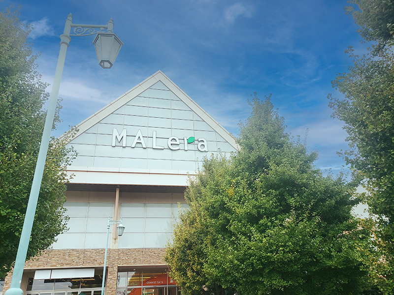 【建物外観】青空を背景にしたモレラ岐阜の正面外観。白い大きな建物と、手前の緑の木々が爽やかな印象を与える。