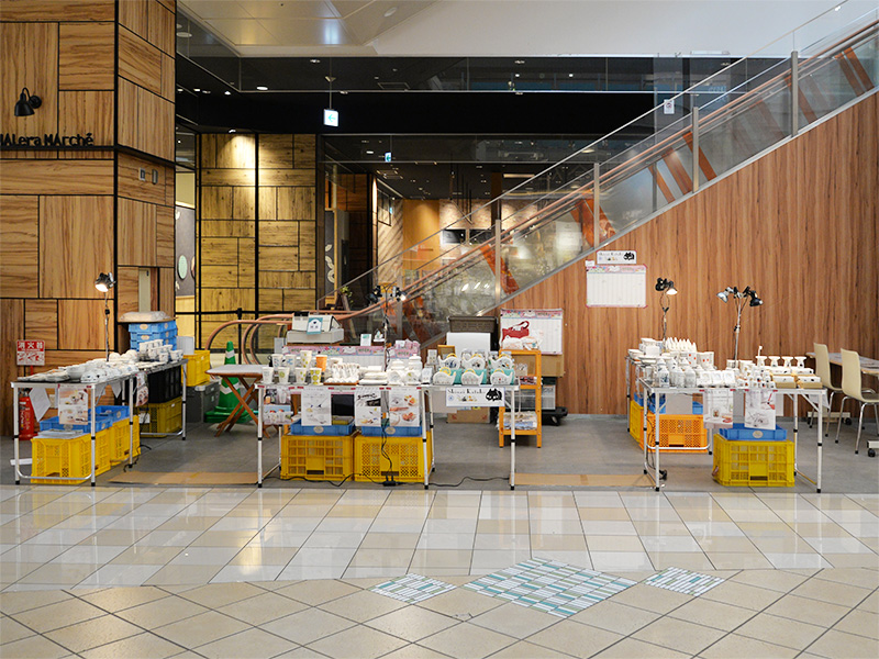 【会場全体】モレラ岐阜・1階催事スペース全景。木目調の壁とエスカレーター横に設置されたゼルポティエの4つのテーブル。賑わいが始まる前のわくわく感が伝わる様子。