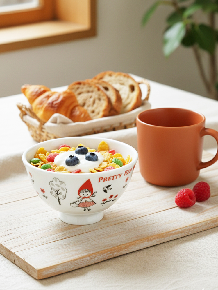 赤ずきんちゃん, お茶碗, 美濃焼, クリスマスプレゼント　白地に赤ずきんちゃんのレトロなイラストが描かれた美濃焼のお茶碗。カラフルなシリアルとヨーグルト、ブルーベリーが盛り付けられ、手前には木製ボードと茶色のマグカップが置かれた温かい朝食の風景。