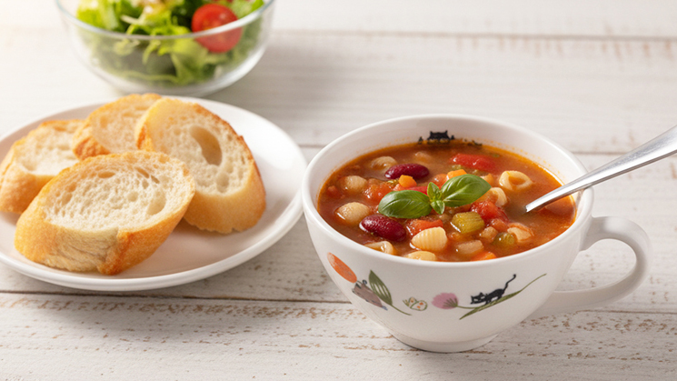 シンジカトウが描く愛らしい猫柄の美濃焼ランチマグ。温かいミネストローネとバゲットが並ぶ食卓の風景。ゼルポティエの新作食器が彩る、心温まるランチタイムのイメージ。