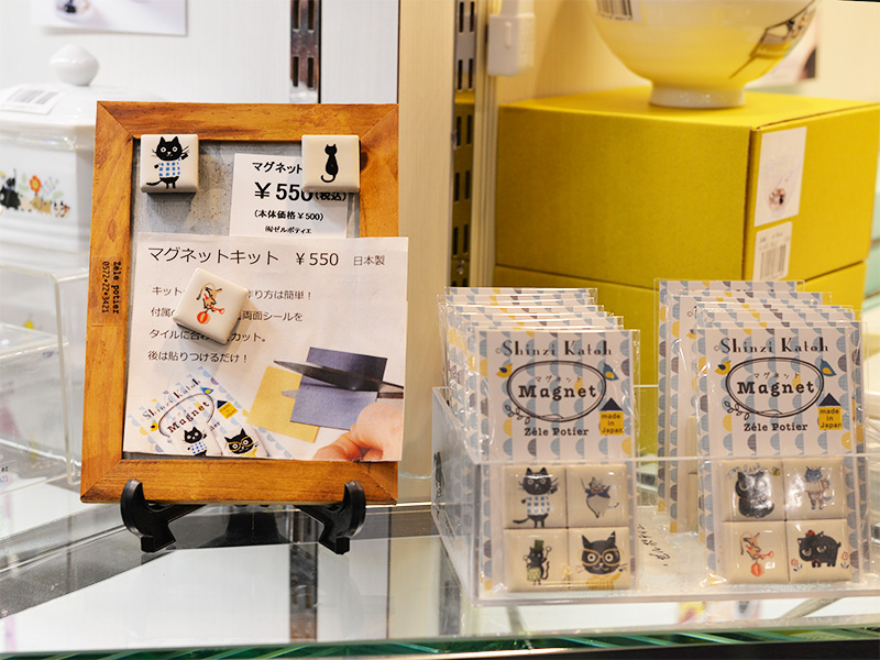 木製のフレームに飾られた猫のタイルマグネット。手作りを楽しめる「マグネットキット」として、四角いタイルに楽器を吹く猫や散歩する猫が描かれ、オフィスや冷蔵庫を猫まみれにできる楽しいアイテムです。