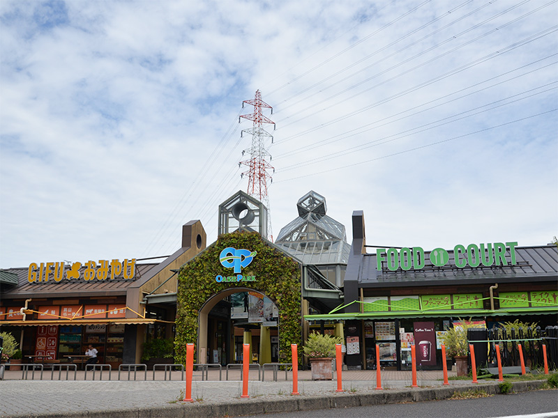 東海北陸自動車道 川島PA（下り）に隣接するオアシスパークの入り口。青空の下、ガラス張りのピラミッド型屋根を持つ特徴的な建物と、緑の蔦に覆われたアーチ、赤い鉄塔が見える。