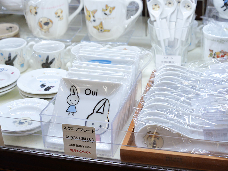 「Designed by Shinzi Katoh（シンジカトウ）」のうさぎ柄スクエアプレート。透明なケースに入っており、青いワンピースを着たうさぎと顔のアップが描かれている。「電子レンジOK」の表記がある。