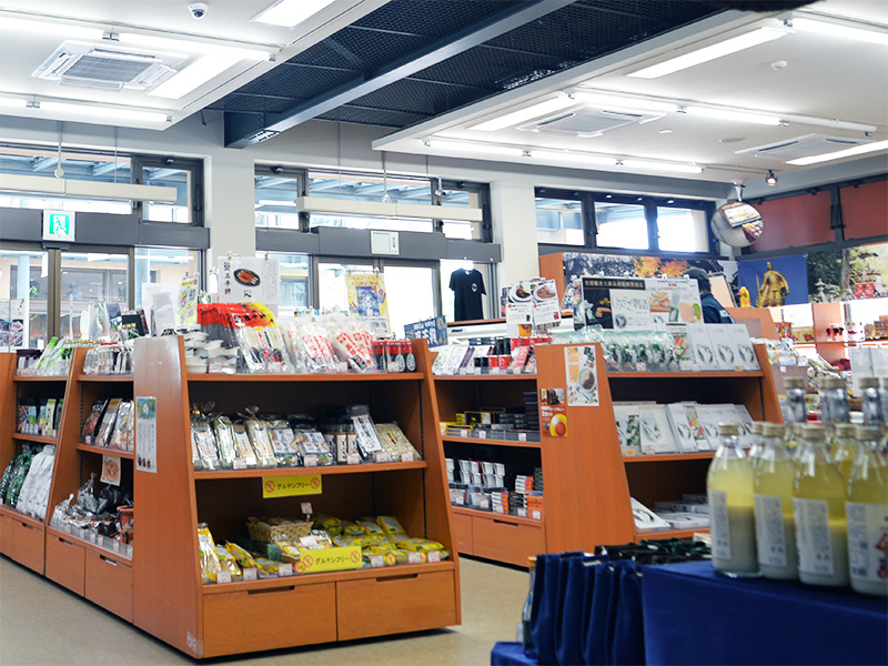 川島PA（下り）の「岐阜おみやげ川島店」店内。木製の棚には岐阜県の名産品や菓子が並び、右側にはShinzi Katoh（シンジカトウ）デザインの可愛い動物柄のマグカップや、電子レンジOKのスクエアプレート、スプーンなどの雑貨が陳列されている。