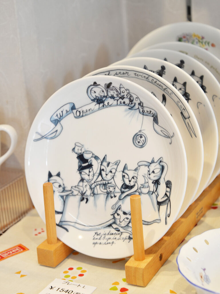 【たじみ陶器まつり】シンジカトウデザイン「ユーモレスク」シリーズの美濃焼プレート。繊細なタッチで描かれた猫たちが、テーブルを囲んでお茶会や読書を楽しんでいる可愛らしいイラスト。落ち着いた色使いの縁取りが、アンティークのような温かみを感じさせる一枚。