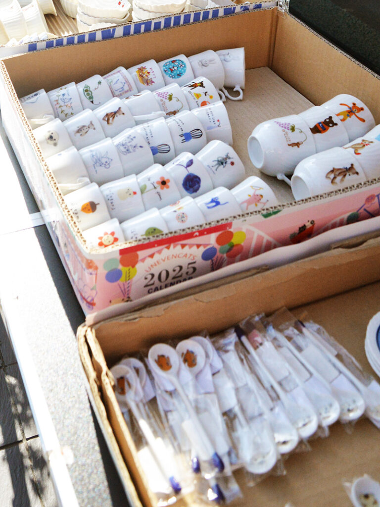 木箱に並べられたシンジカトウデザインのマグカップとスプーン。うさぎやクマなどの動物柄が描かれた温かみのある美濃焼の食器。