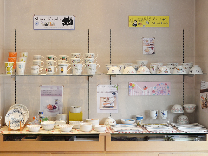 たじみ陶器まつり】老舗呉服店の店内に設けられた、ゼルポティエの特設展示棚。木製の多段棚には、シンジカトウがデザインしたクマやウサギなどの動物柄のマグカップ、カラフルな小皿、ボウルといった美濃焼の器がずらりと並び、奥では来場者が楽しそうに器を選んでいる。