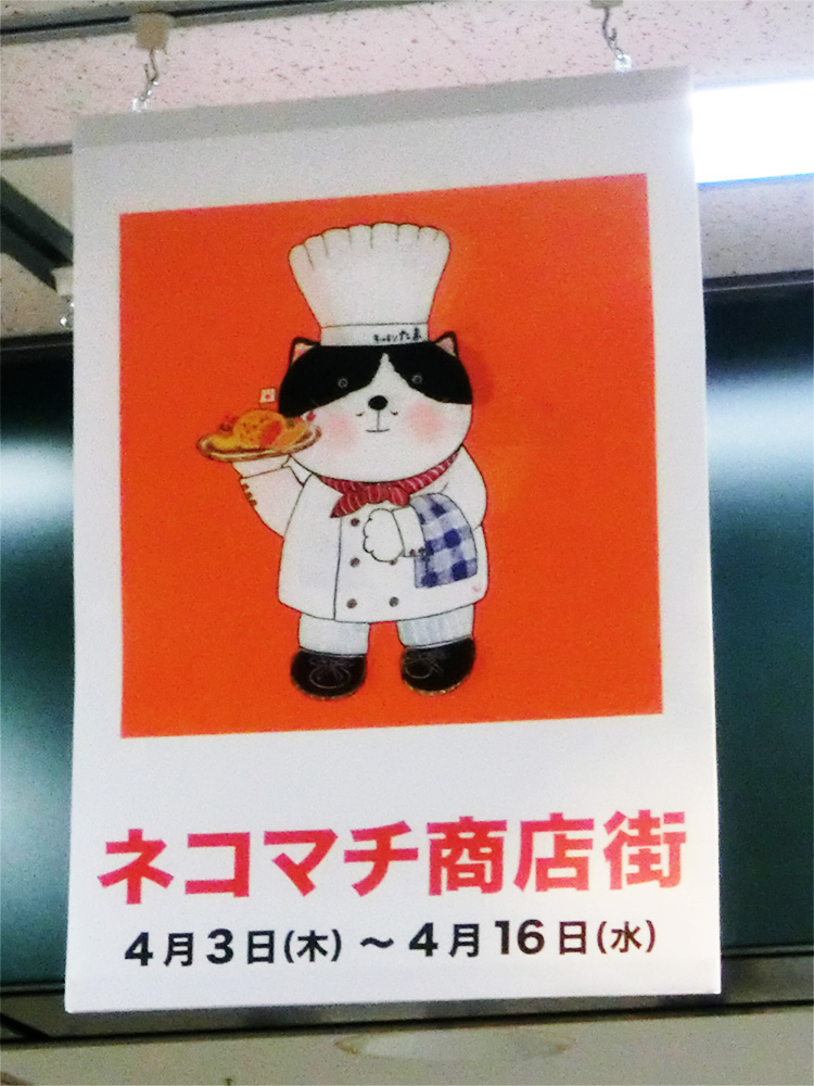 過去のイベント会場。コック帽をかぶりオムライスを運ぶ可愛い猫シェフのバナーが吊り下げられた賑やかな売場風景。