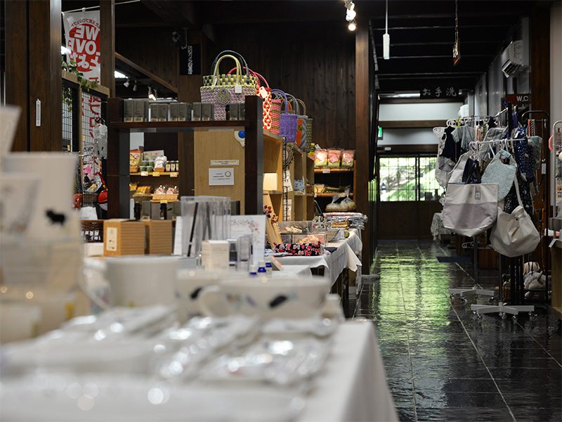 10月2日に「香恋の館」へ商品補充を行った際の店内全景。手前にはDesigned by Shinzi Katoh(シンジカトウ)の陶器の器やマグカップが並び、奥に広がる磨き上げられた床の通路沿いにはカラフルな手編みバッグやハンドメイド服・雑貨がずらりと並べられています。