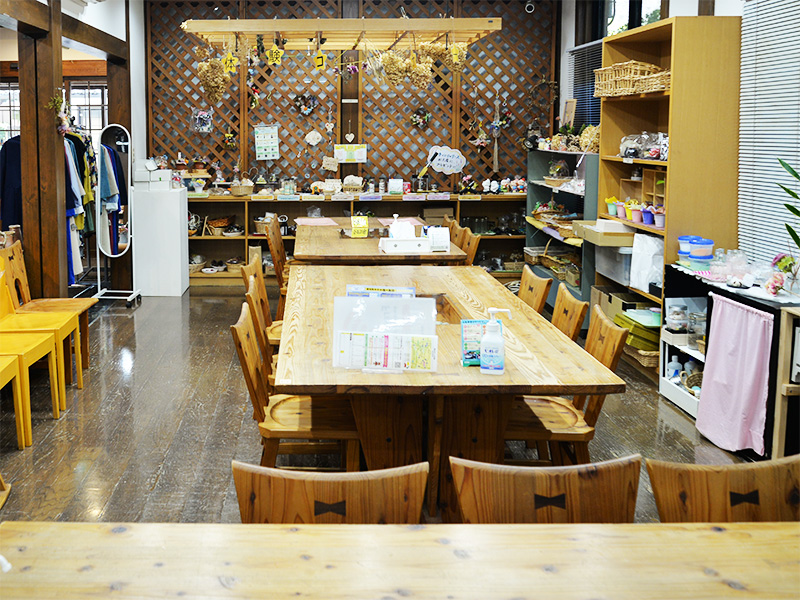 10月2日に「香恋の館」へ商品補充に訪れた際の体験工房スペース。温かみのある大きな木製長テーブルと椅子が並び、天井からはドライフラワーがつるされています。壁際の格子棚にはクラフト作品や体験用の材料が整然と配置され、木の温もりあふれる広々とした空間です。